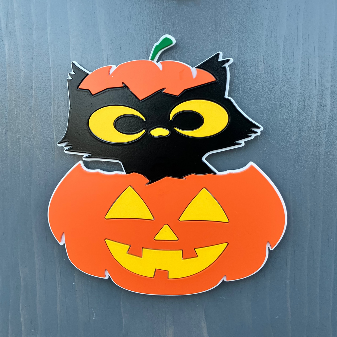 Halloween-themed decorative sign with a black cat in a pumpkin on a gray background.